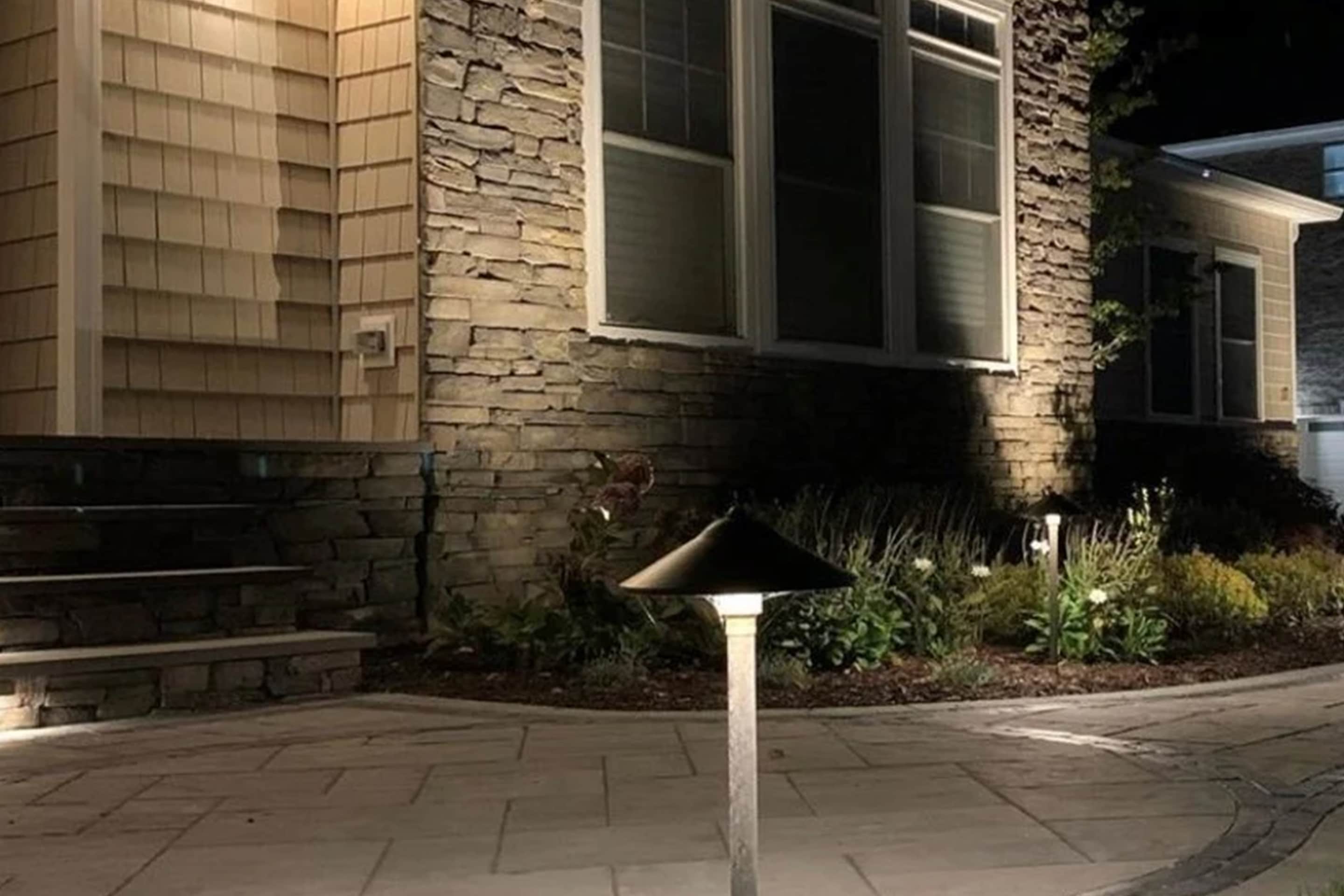 A sample of Vision Landscape Services hardscape design - first floor exterior view of a house with stone work illuminated and walkway lights
