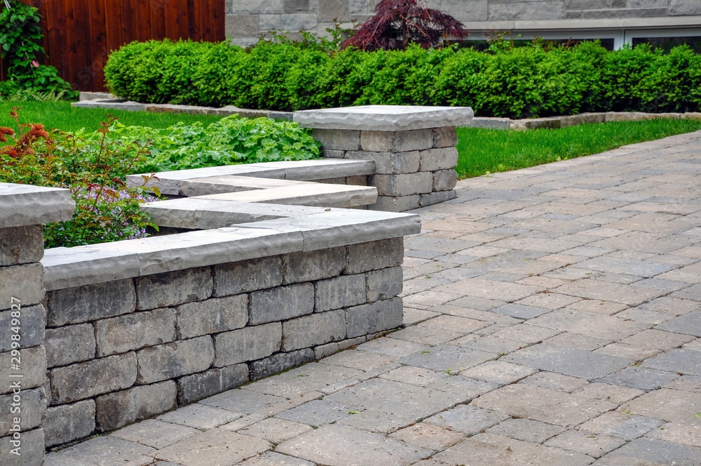A sitting wall with pillars and natural stone coping helps define a tumbled paver driveway and is a beautiful landscaping feature.