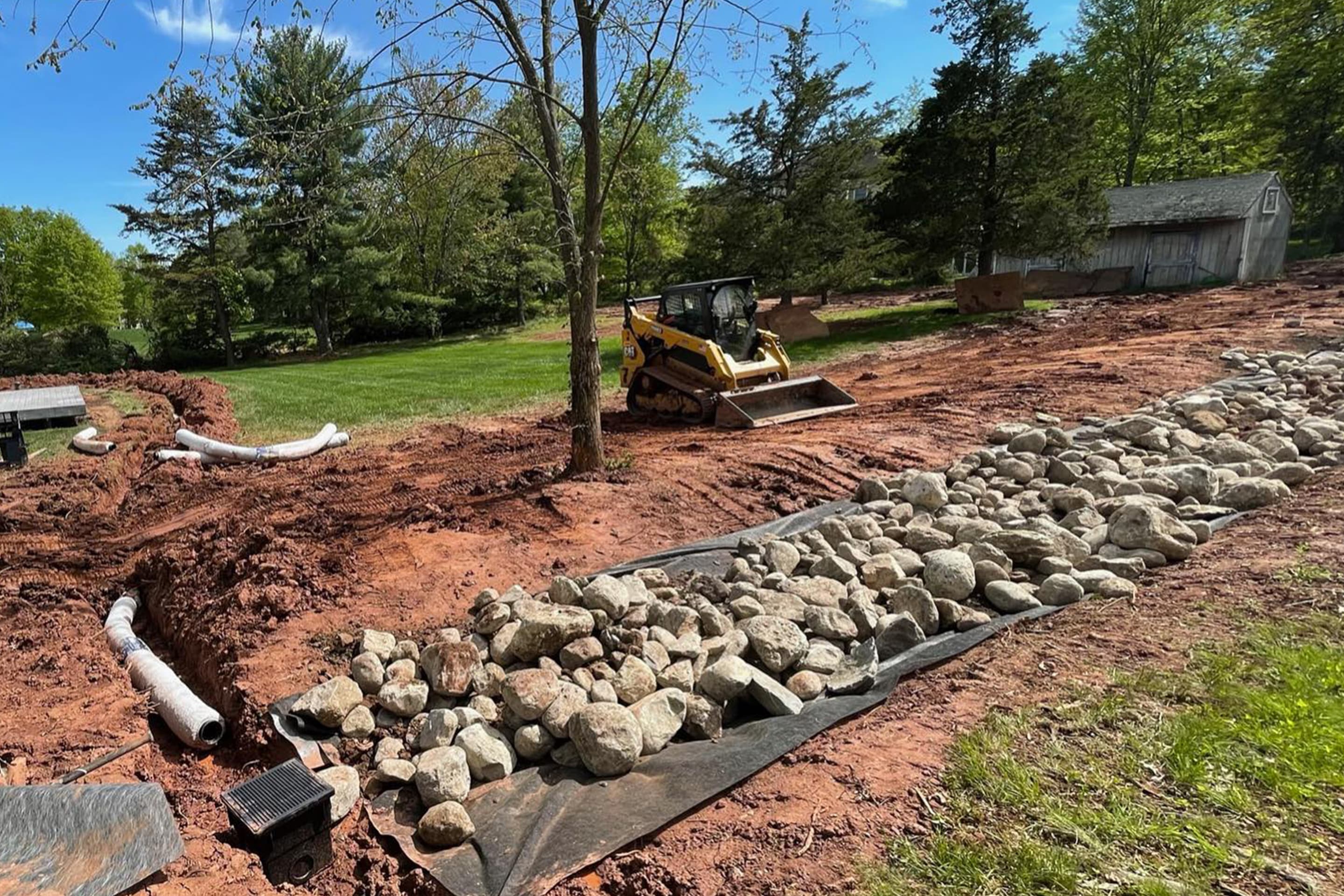 Vision Landscape Services excavates a ditch to install a drainage system of pipes and rocks to ensure proper water runoff.